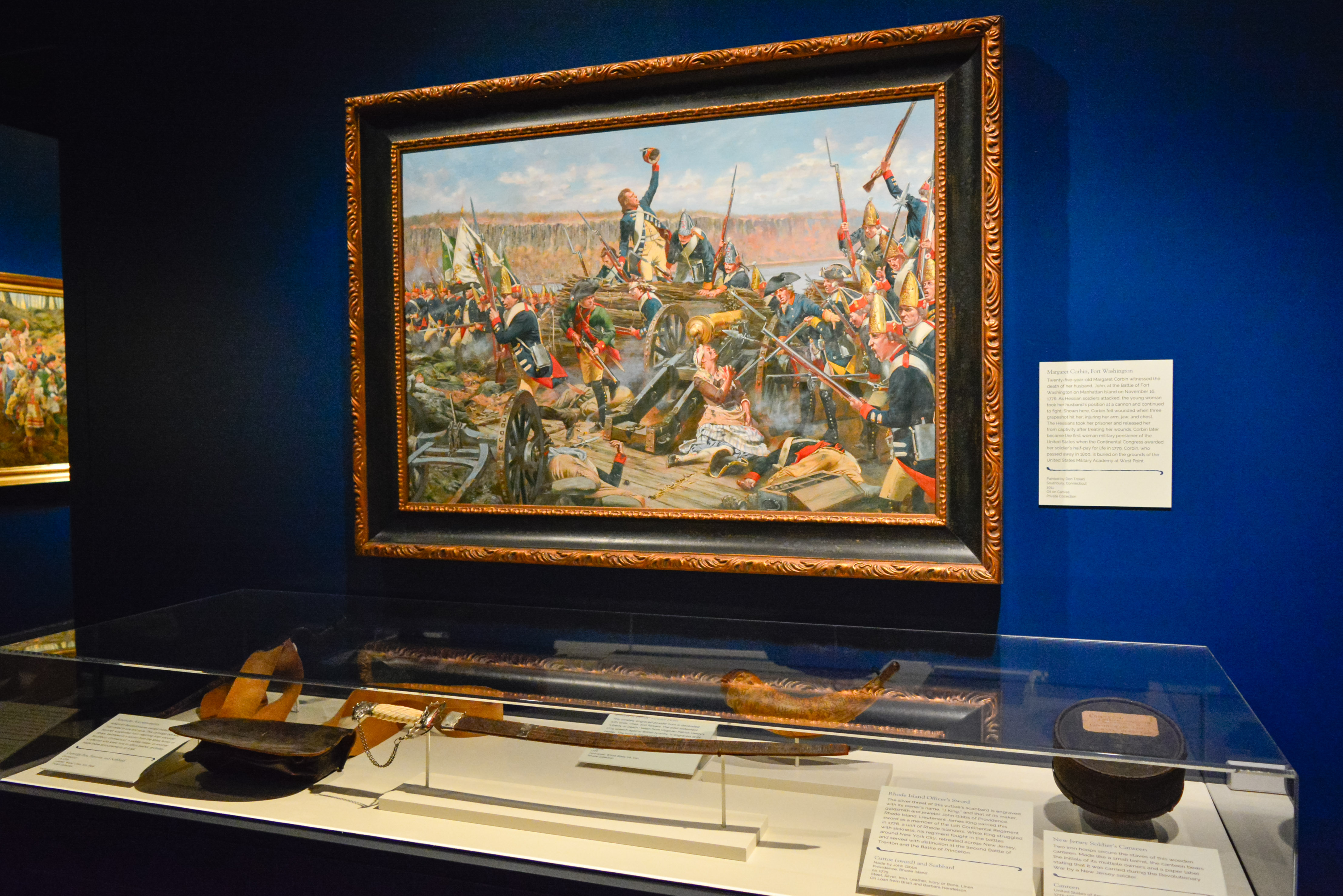 A painting hangs above a display case of corresponding artifacts in the Liberty exhibit.