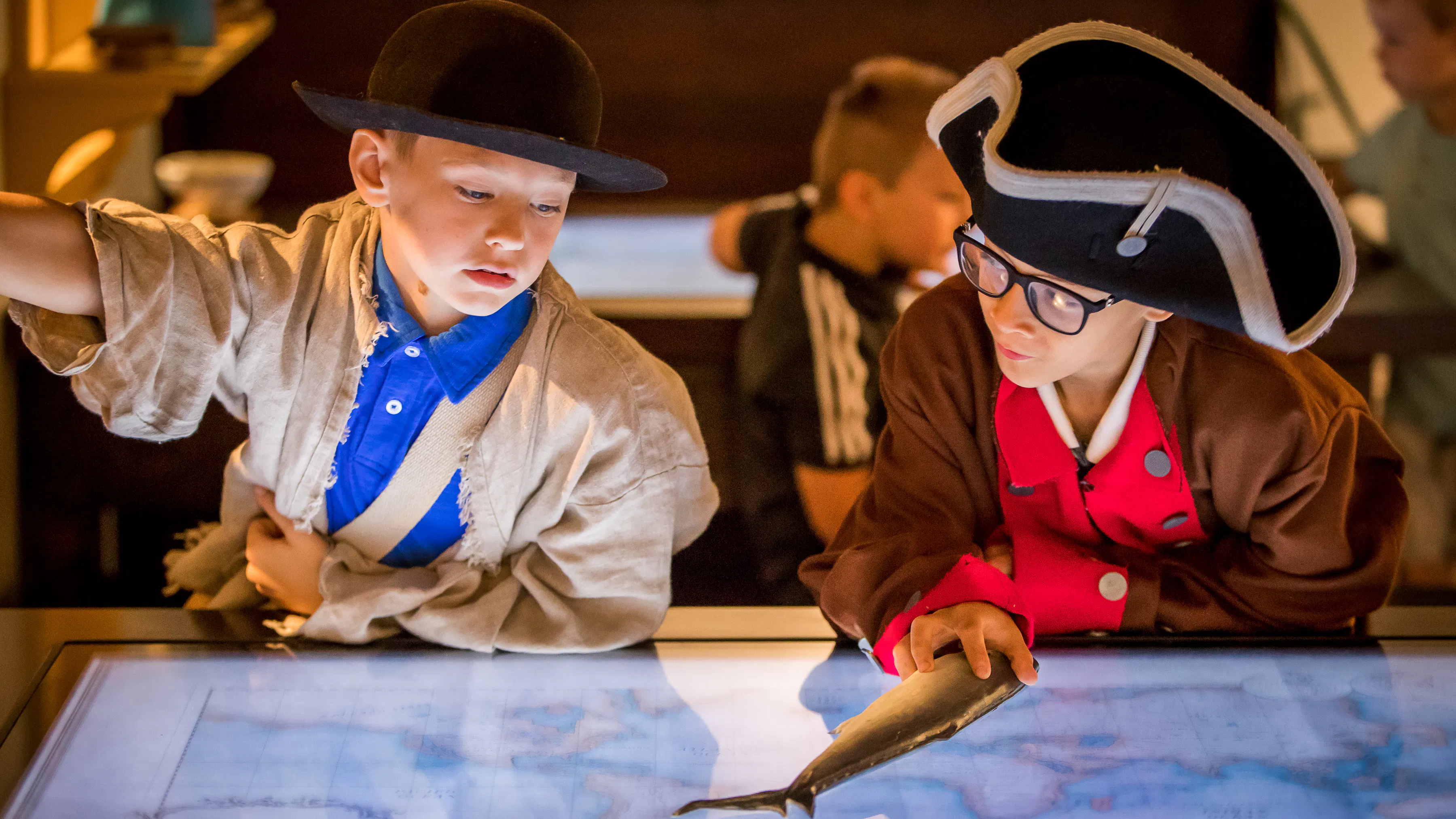 Two male adolescents interactive with a digital map in Revolution Place. They are both dressed in Revolutionary-era clothing.