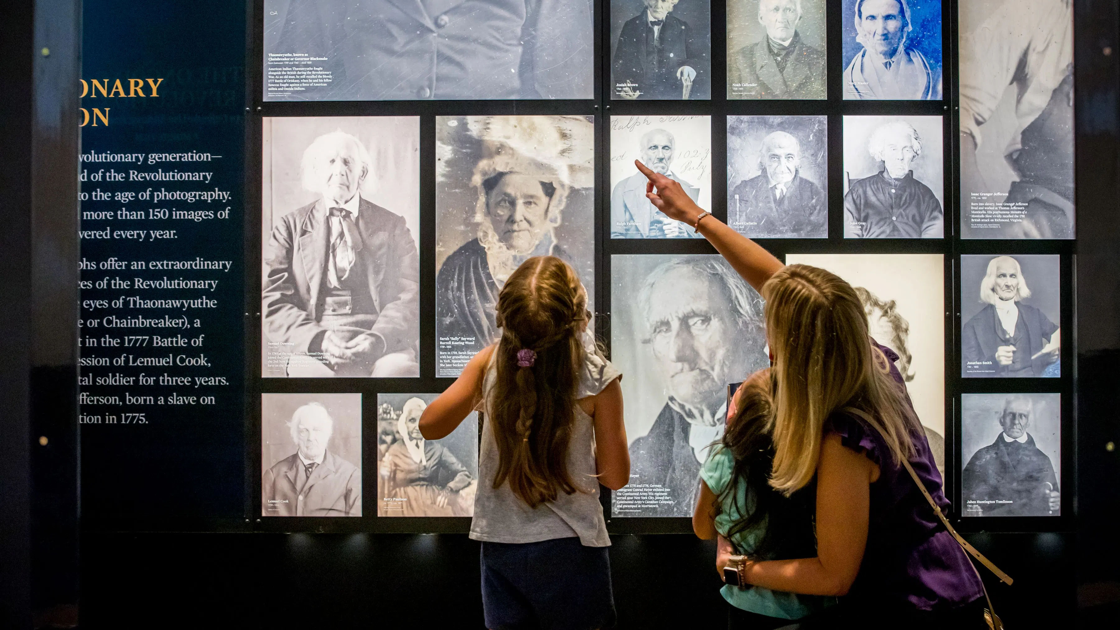 A mother and two young daughters look at photos on the Revolutionary Generation Wall at the Museum.