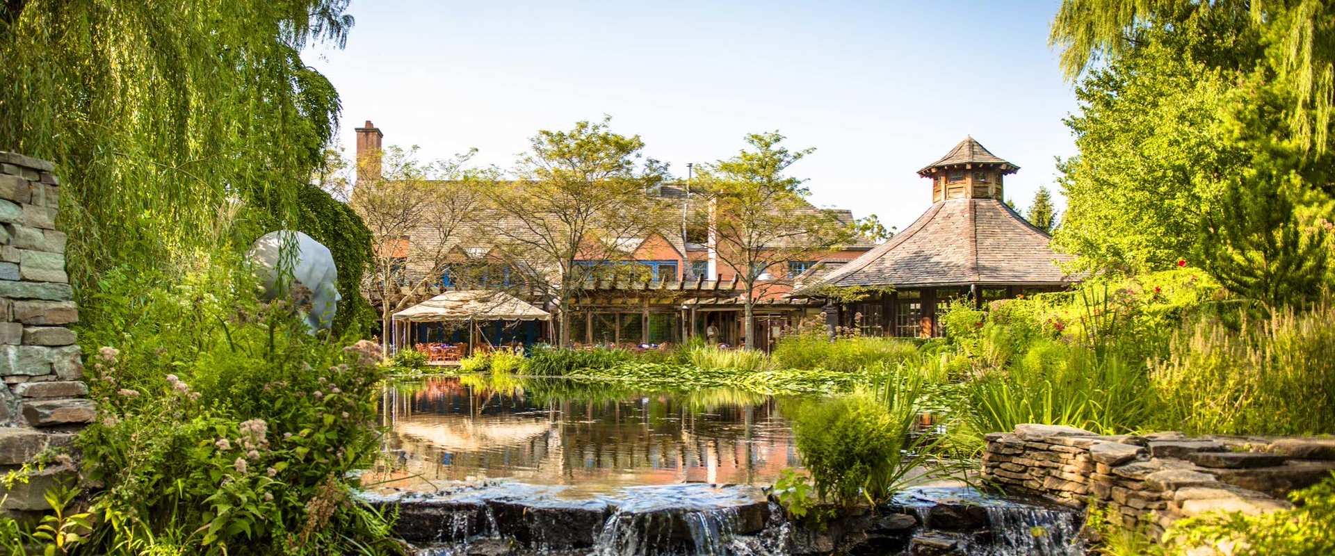 This image shows a pond, greenery, and wooden building that's part of Grounds for Sculpture in New Jersey.