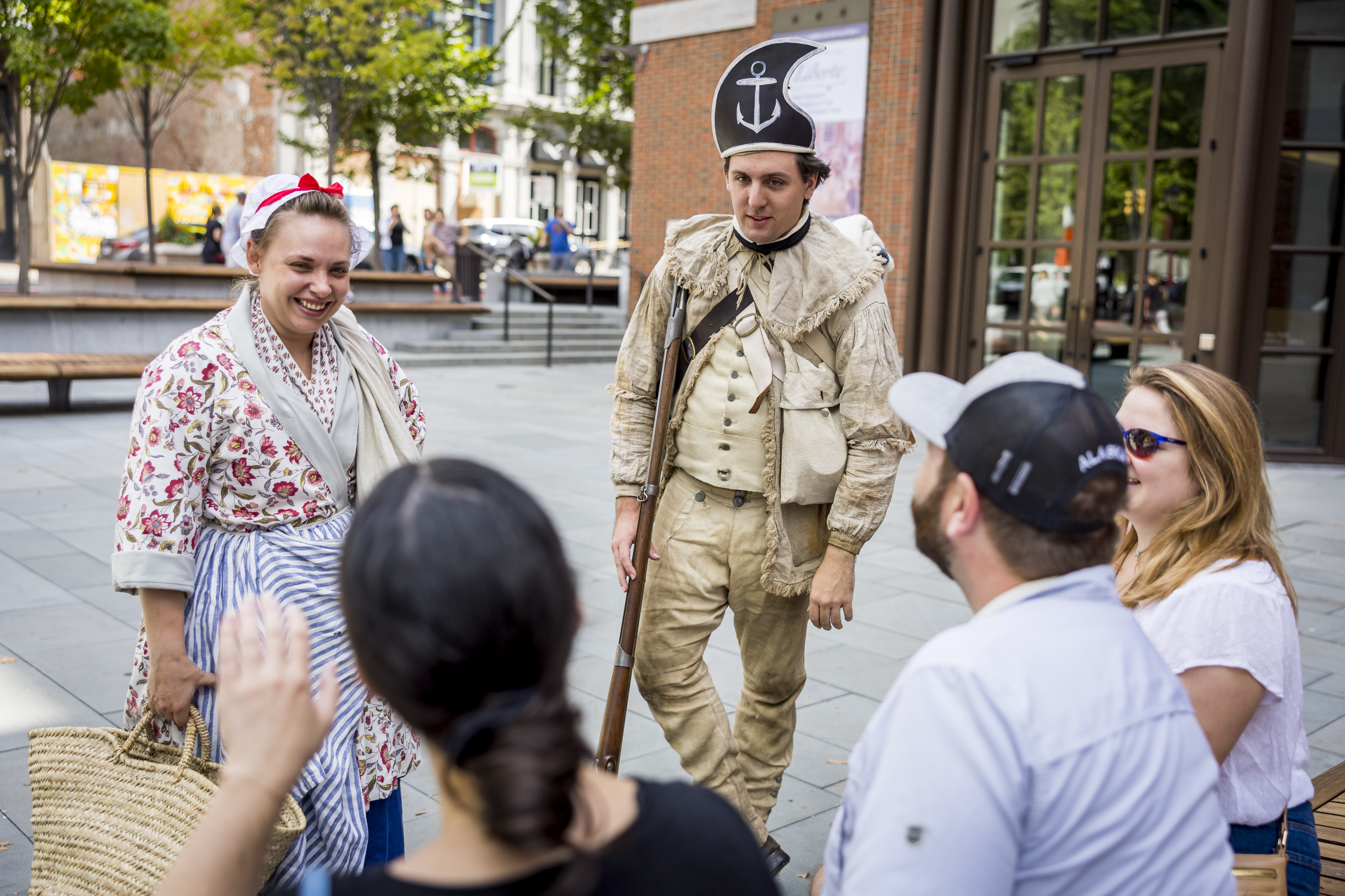 Two living history interpreters talk with a group of visitors on the Museum's outdoor plaza.