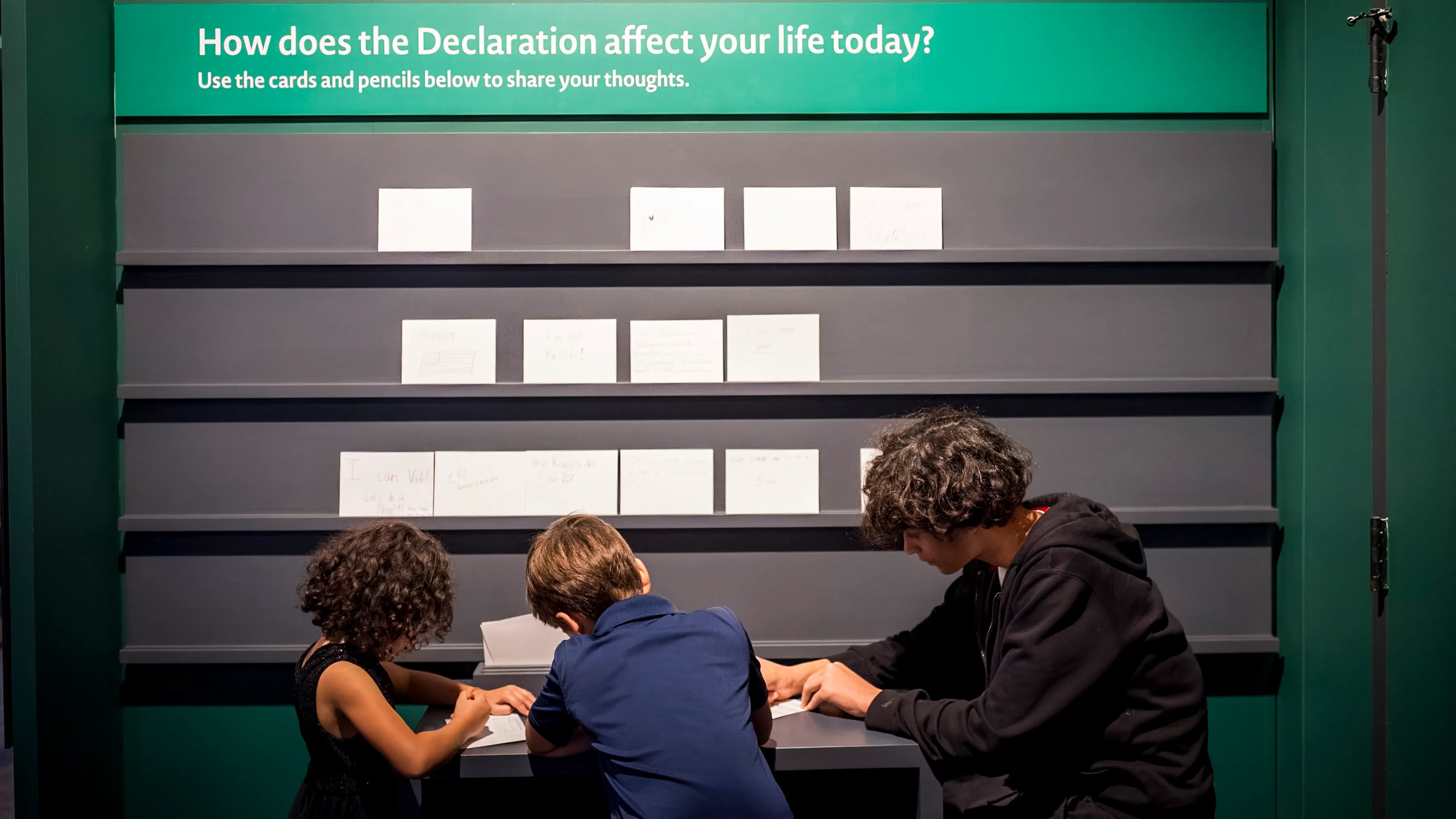 People sit writing in front of the talk-back wall