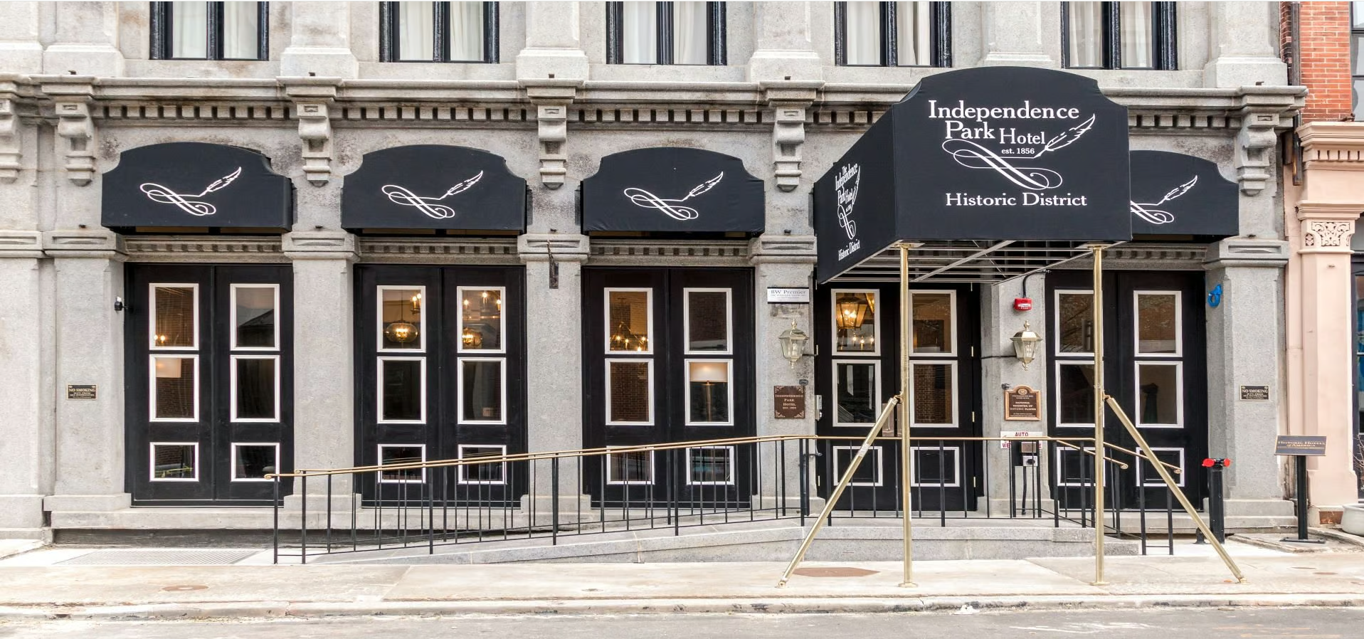 This image shows the white-gray facade with black details of the Independence Park Hotel across the street from the Museum.