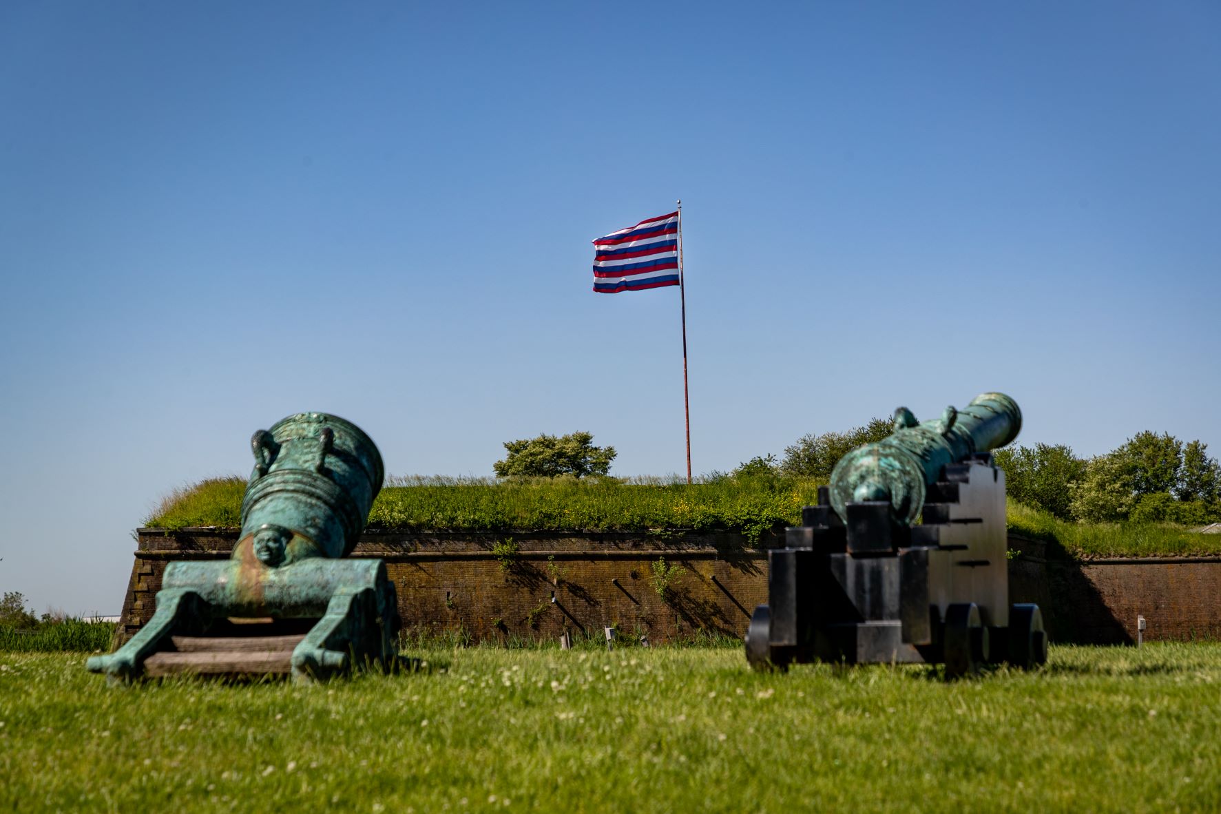 This image shows a cannon in the foreground with a flag with traditional red white and blue stripes waving in the background.