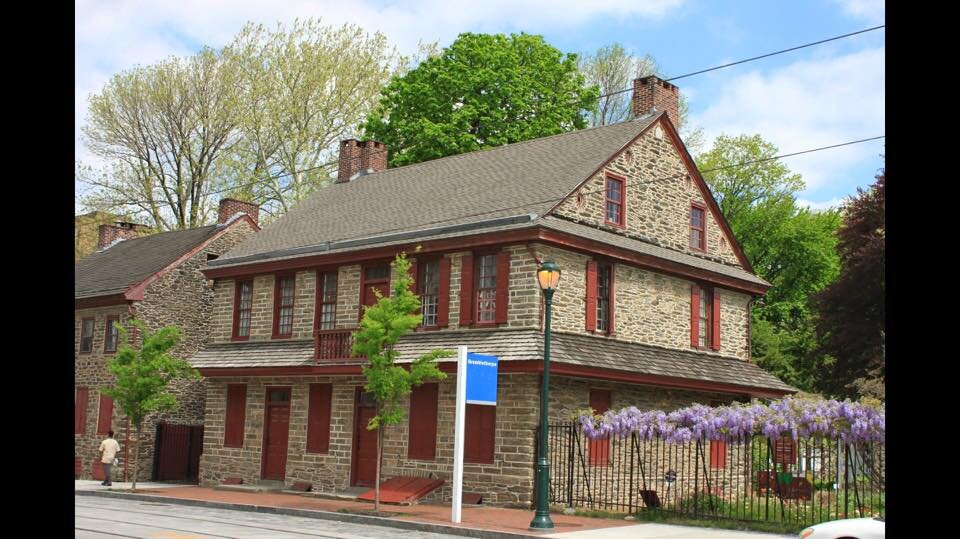 This image shows a beige stone house with red shutters and details in Germantown.