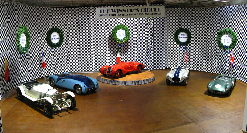 This image shows five classic cars with colors left to right of white, blue, red, white with a black stripe down the center, and green.