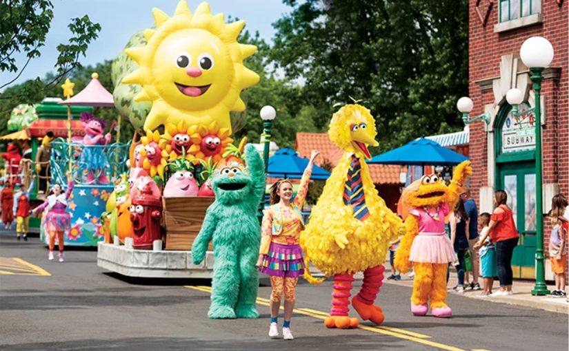 This image shows Big Bird leading a parade of Sesame Street characters and floats at Sesame Place.
