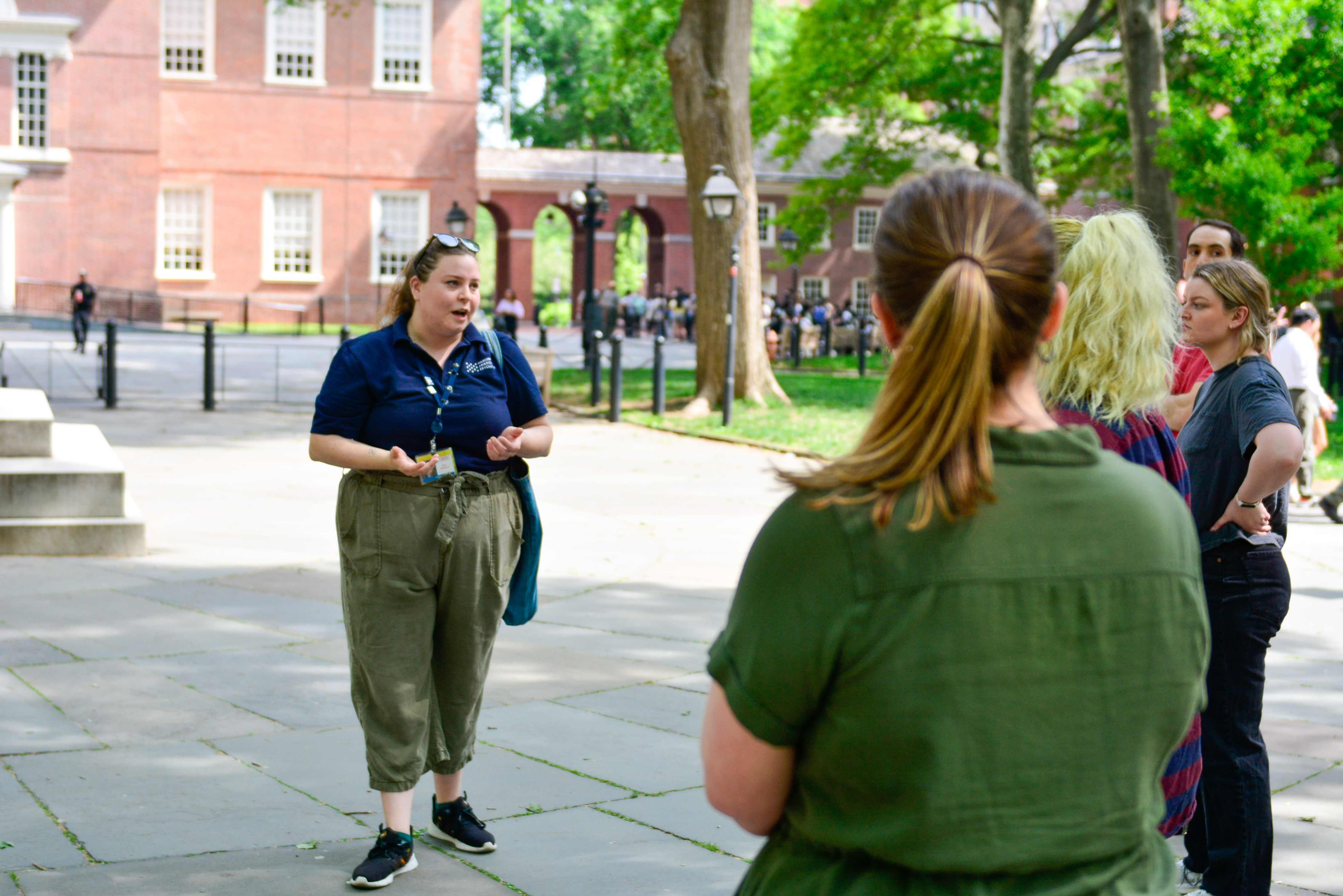 A Museum educator talks to people in front of Independence Hall