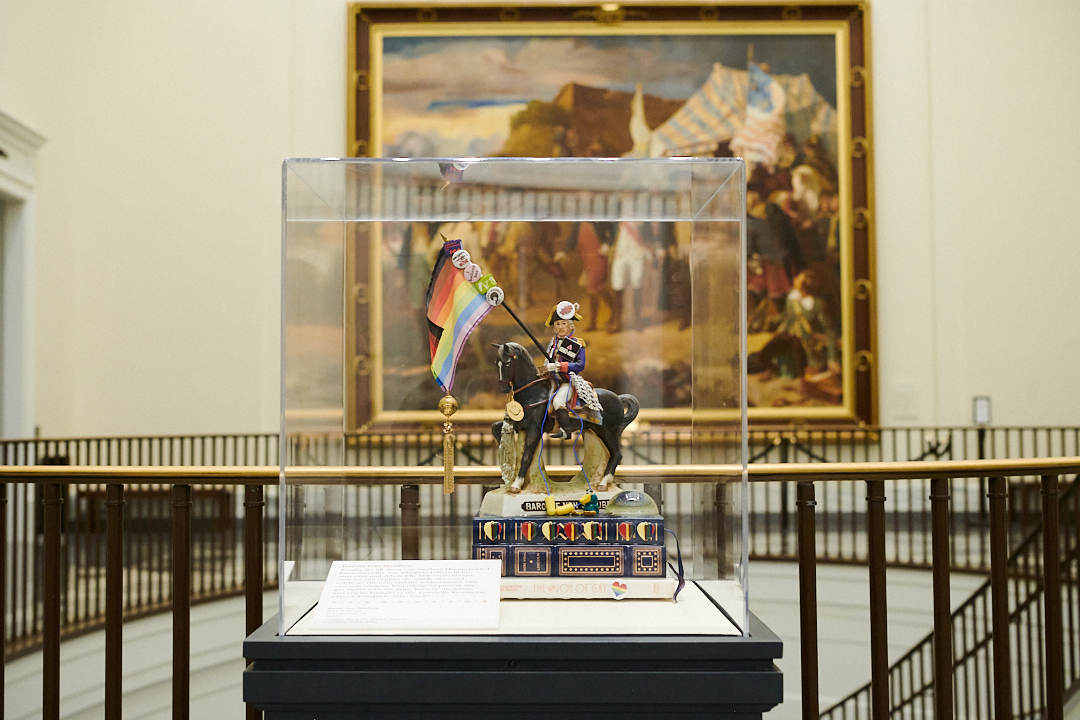 A sculpture of a man on horseback holding a Pride flag. The horse stands on top of a stack of books.