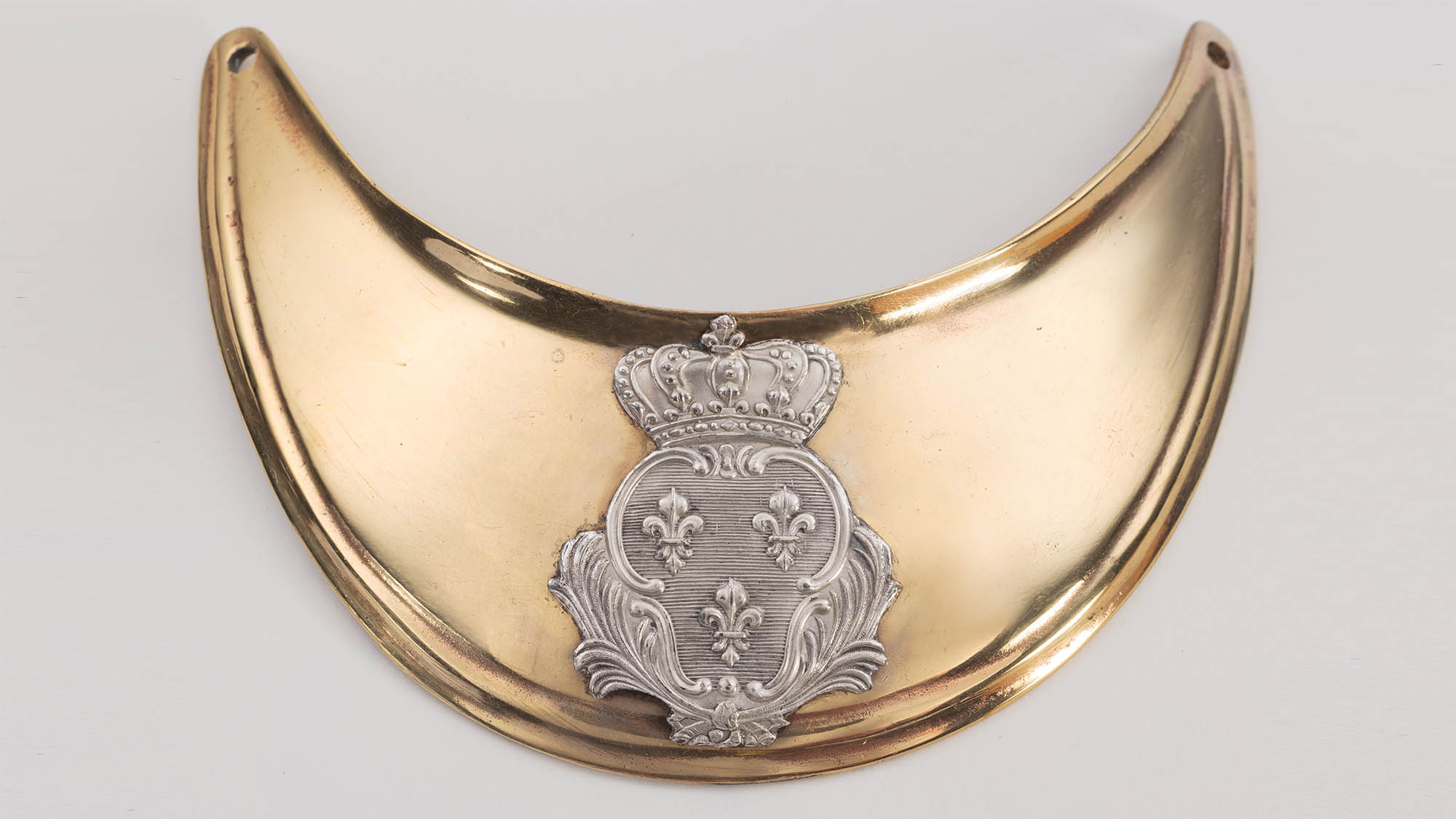This image shows a French gorget. It is gold with a silver crown symbol in the center. It is displayed against a white background.