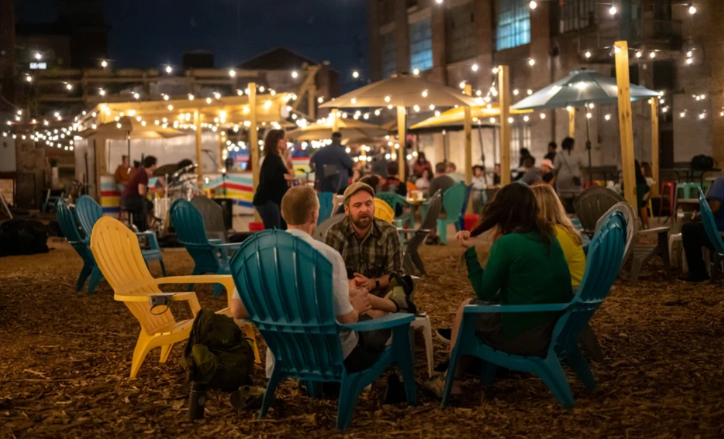 This image shows people sitting in Adirondack chairs under string lights in an outdoor beer garden at Attic Brewing Company.