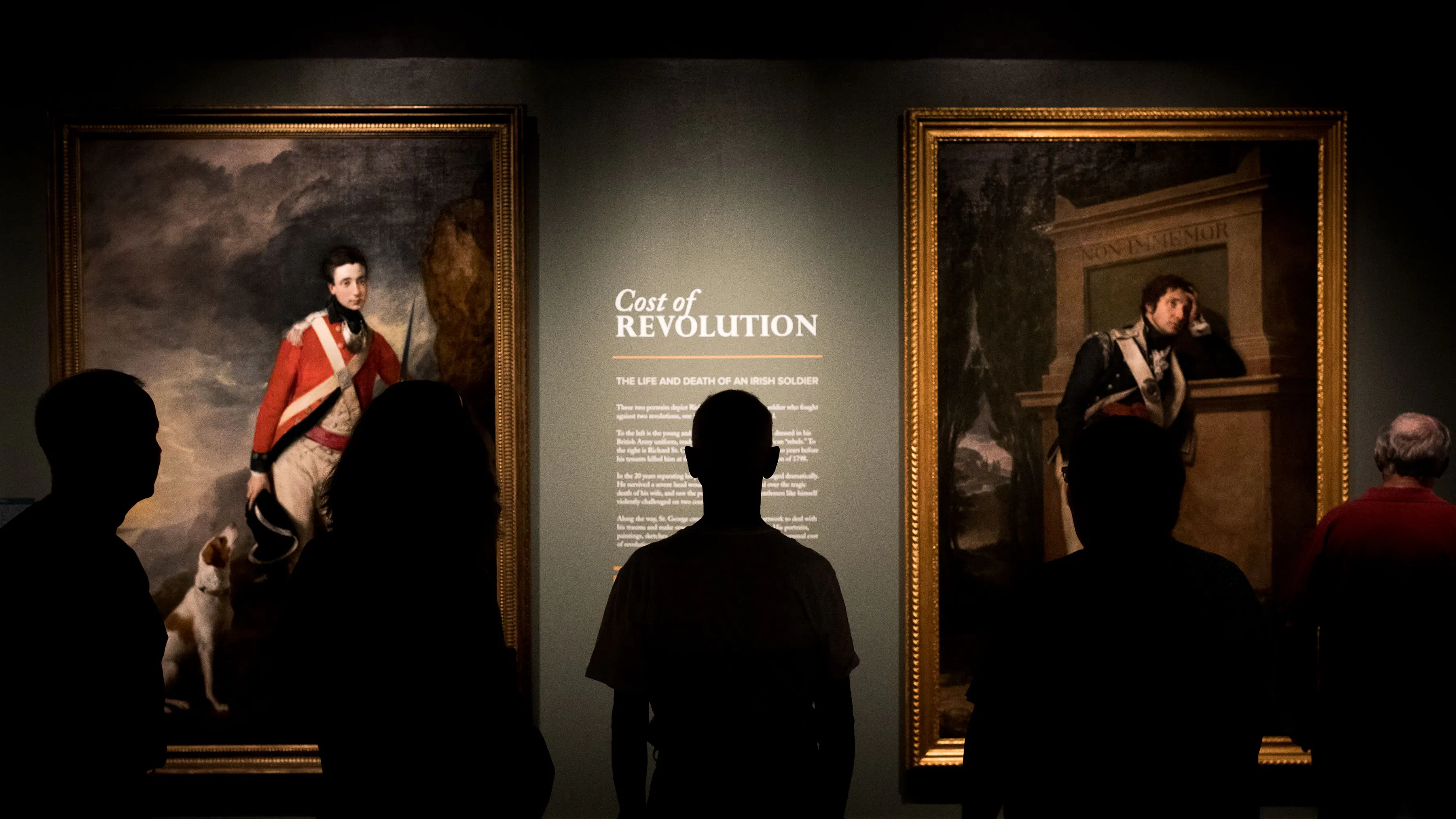 Museum visitors look at wall text that reads "Cost of Revolution"