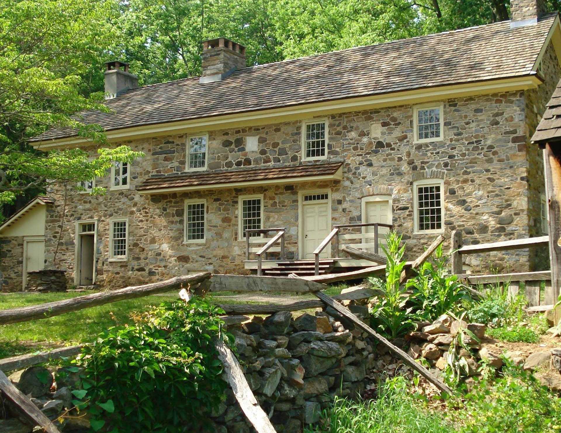 This image shows an old stone home with a wooden fence out front that is the Colonial Pennsylvania Farmstead.