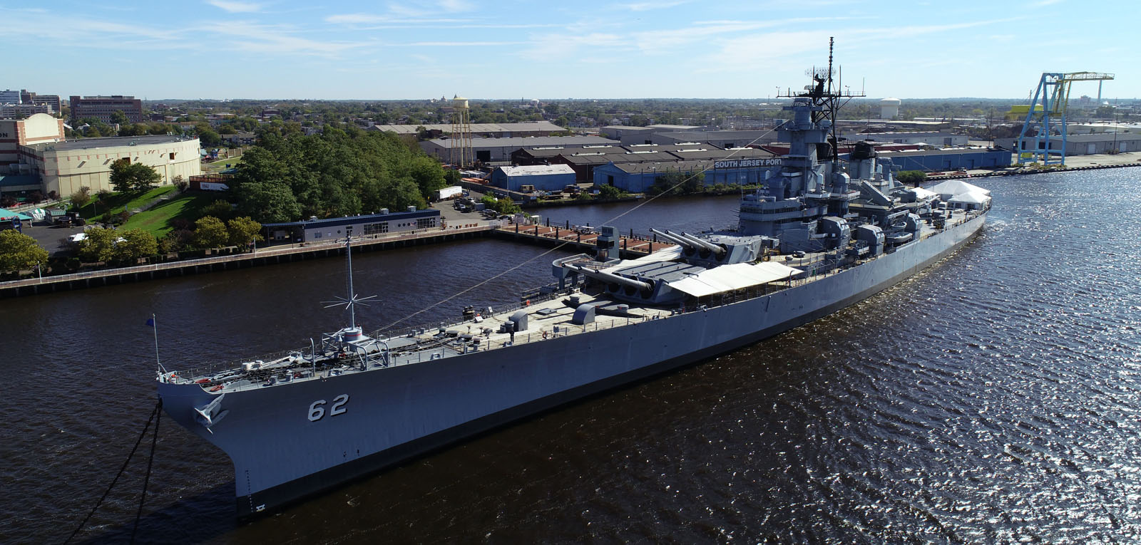 This image shows an aerial photograph of the Battleship New Jersey, a long deep gray naval ship.