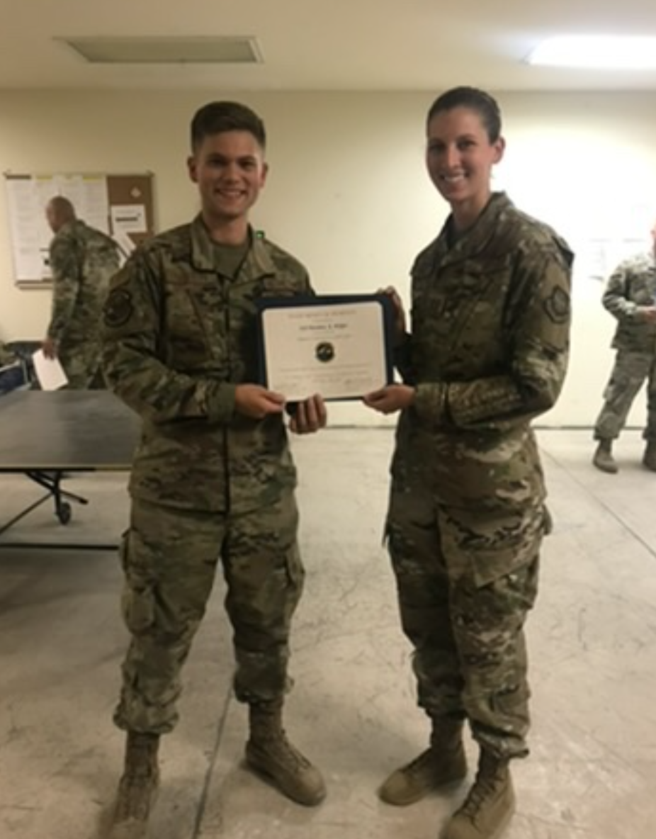 Matthew Midget, wearing camo military gear, receives a military certificate.