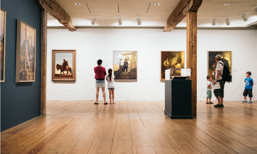 This image shows visitors looking at paintings hung in a gallery space at the Brandywine River Museum of Art.